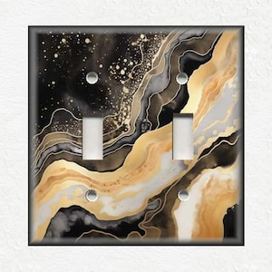 May include: A double light switch cover with a black, gold, and white abstract design. The design features swirling lines and dots.