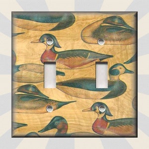 May include: A light switch cover with a vintage illustration of ducks on a woodgrain background. The ducks are painted in shades of blue, green, and brown.