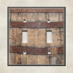 May include: A light switch cover with a rustic wood grain design. The cover has two switch openings and is made to look like a weathered wooden barrel.