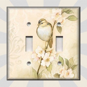 May include: A light switch cover with a watercolor design of a small bird perched on a branch with white flowers. The background is a light beige with a subtle floral pattern.