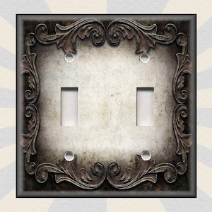 May include: A decorative light switch cover with a distressed, aged look. The cover features an ornate, intricate design with a dark brown finish. The switch plate has two toggle switches.