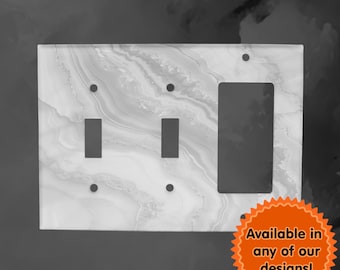 Puede incluir: Una placa de interruptor de luz blanca con patrón de mármol, dos interruptores de palanca y una toma de corriente simple. Disponible en cualquiera de nuestros diseños!