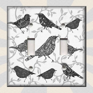 May include: A decorative light switch cover featuring a pattern of black and white birds with intricate designs. The birds are perched on gray branches against a white background. The cover has two switch openings.