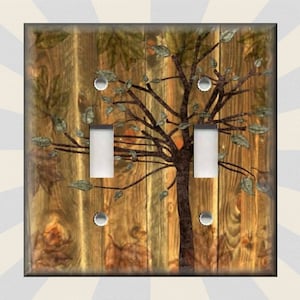 May include: A double light switch cover with a rustic wood background and a stylized tree with leaves in shades of brown, green, and orange.
