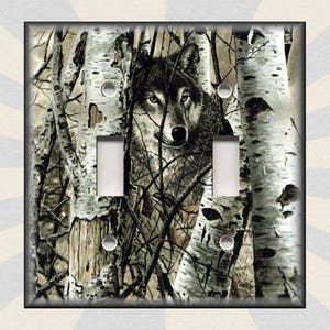 May include: A light switch cover featuring a black and white wolf peering through a forest of birch trees. The wolf's eyes are a piercing blue.
