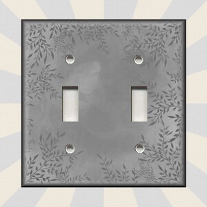 May include: A gray light switch cover with a white floral pattern. The cover has two toggle switches and two screw holes.