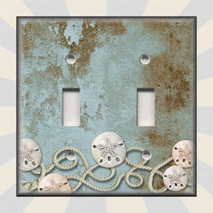 May include: A light blue double light switch cover with a distressed, weathered look. The cover features a design of white rope and sand dollars on a blue background.