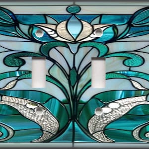 May include: A decorative light switch cover with a stained glass design. The cover features a floral pattern in shades of teal, white, and silver. It has four light switch openings and a rectangular shape.