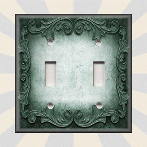 May include: A double light switch cover with a decorative, ornate, green metal frame. The frame has a distressed, aged look with a light green background.