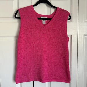 May include: A sleeveless pink sweater with a V-neck. The sweater is made of a textured knit fabric.