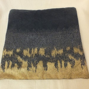 May include: A black and gold decorative pillow with a textured woven design. The pillow has a dark gray band in the middle.