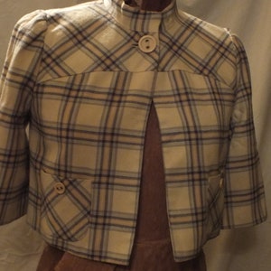 May include: A white and blue checked cropped jacket with a mandarin collar and two pockets. The jacket has a brown lining and is on a dress form.
