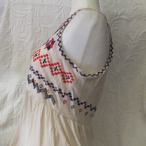 May include: A white sleeveless dress with a geometric pattern embroidered on the bodice in red, blue, and purple.