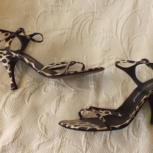 May include: A pair of high-heeled sandals with a leopard print pattern. The open-toe shoes have thin straps and a stiletto heel. The heels are approximately 3 inches tall.