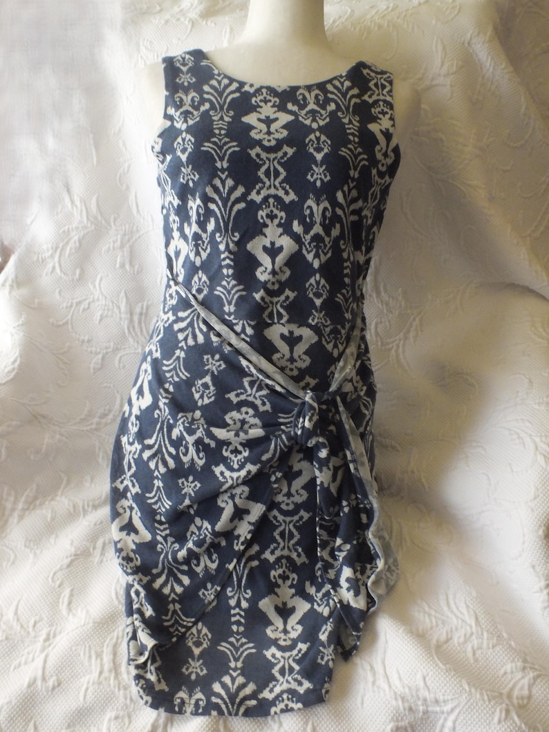May include: Sleeveless navy blue dress with a white damask pattern. The dress features a knotted waist detail and a scoop neckline. The fabric has a soft drape, and the dress is displayed on a mannequin.