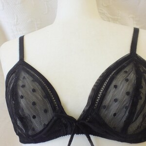 May include: Black lace bralette with polka dots. The bralette has adjustable straps and a tie closure at the center.
