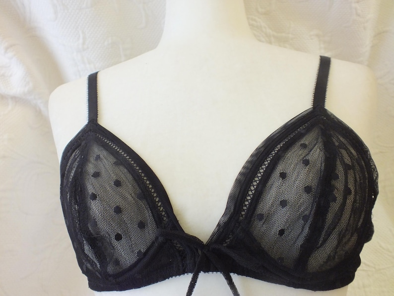 May include: Black lace bralette with polka dots. The bralette has adjustable straps and a tie closure at the center.