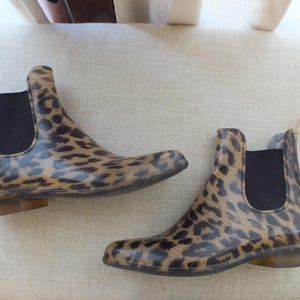 May include: A pair of ankle-high rain boots with a leopard print pattern. The boots have a black elastic side panel and a pull tab at the back. The soles are a light brown color.