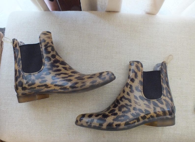 May include: A pair of ankle-high rain boots with a leopard print pattern. The boots have a black elastic side panel and a pull tab at the back. The soles are a light brown color.
