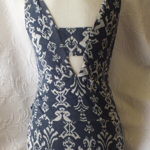May include: A sleeveless, form-fitting dress with a blue and white patterned design. The dress features a V-neckline and a unique back design. The fabric has a repeating floral and geometric pattern. The dress is displayed on a mannequin.