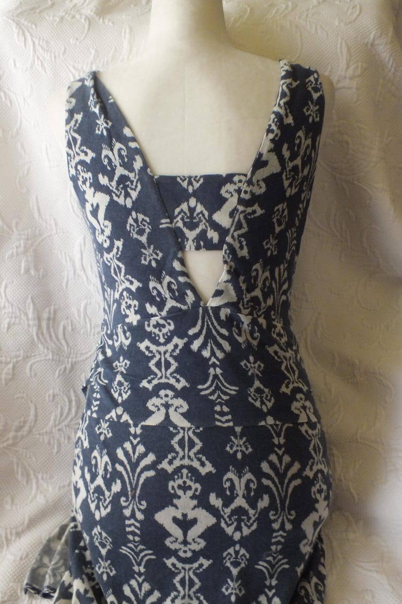 May include: A sleeveless, form-fitting dress with a blue and white patterned design. The dress features a V-neckline and a unique back design. The fabric has a repeating floral and geometric pattern. The dress is displayed on a mannequin.