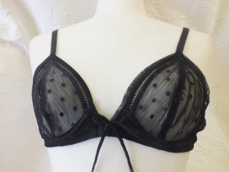 May include: Black lace bra with polka dots. The bra has adjustable straps and a tie closure in the front.