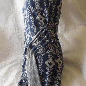 May include: A sleeveless, navy blue dress with a white damask pattern. The dress features a draped, knotted detail at the waist. The fabric appears soft and flowing, ideal for a summer or spring wardrobe.