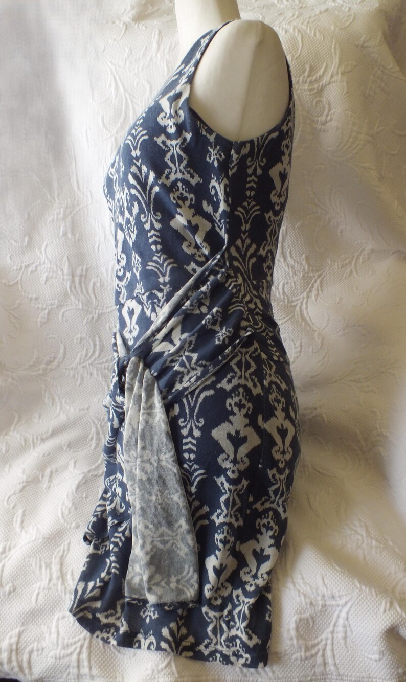 May include: A sleeveless, navy blue dress with a white damask pattern. The dress features a draped, knotted detail at the waist. The fabric appears soft and flowing, ideal for a summer or spring wardrobe.