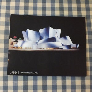 May include: A black and white photograph of the Walt Disney Concert Hall in Los Angeles, California. The building is made of stainless steel and has a unique, modern design. The image is commissioned by LA Phil.