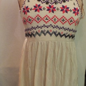 May include: A sleeveless white dress with a geometric pattern in shades of red, pink, purple, and black. The pattern is embroidered with sequins and beads.