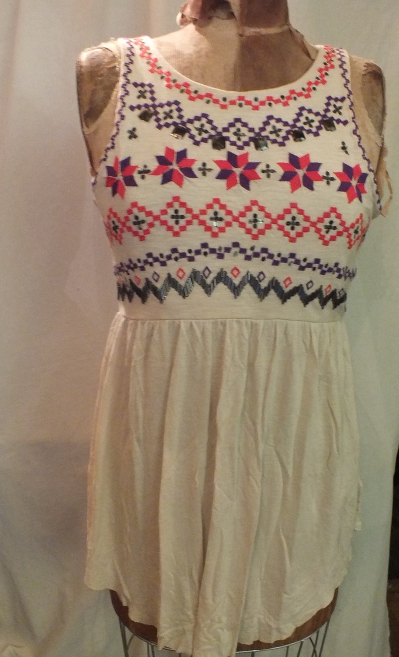May include: A sleeveless white dress with a geometric pattern in shades of red, pink, purple, and black. The pattern is embroidered with sequins and beads.