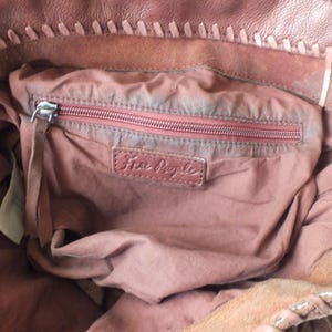 May include: Close-up of a brown leather tote bag interior. The bag features a zippered pocket with a red zipper and a leather tag that reads "Free People". The bag's interior is a dusty rose color.