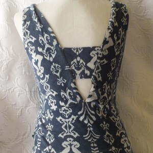 May include: A sleeveless dress with a blue and white patterned design. The dress features a unique back with a cutout and a V-neckline. The fabric has a detailed, repeating floral and geometric pattern.