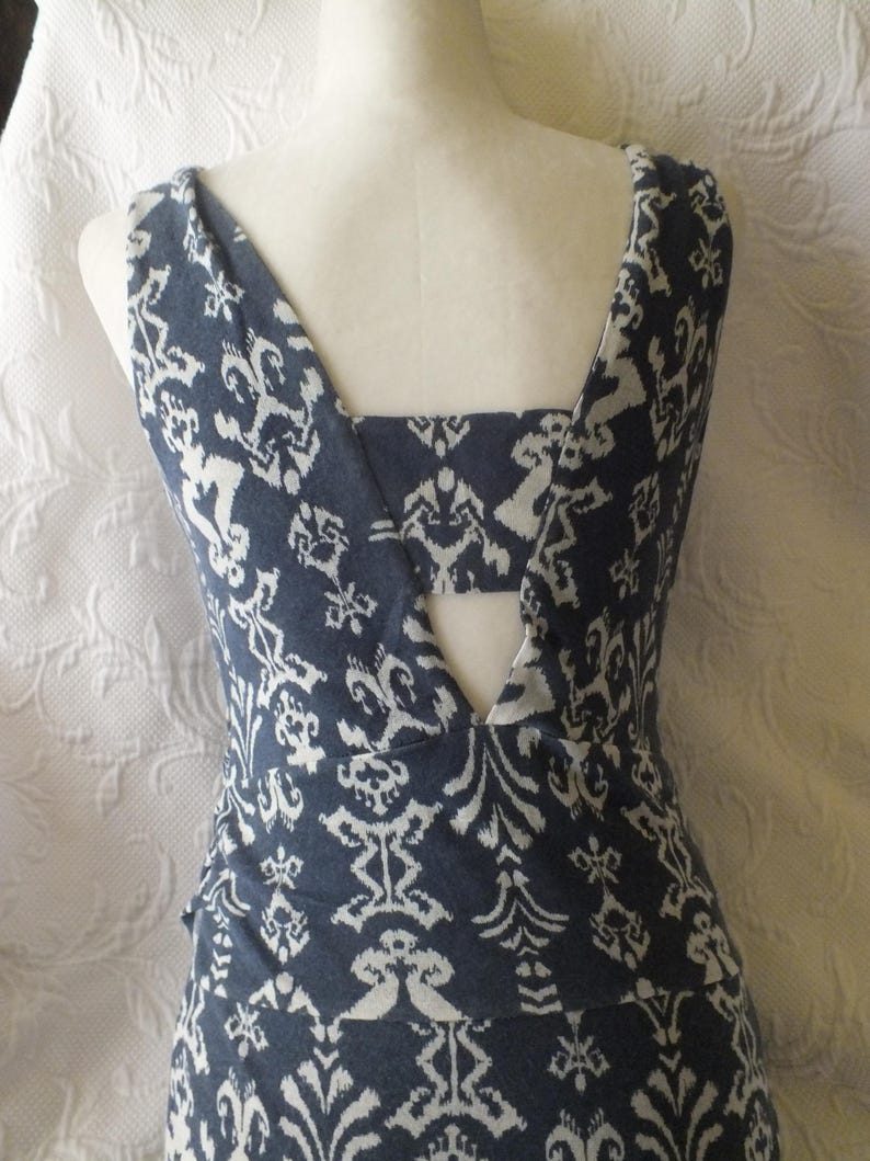 May include: A sleeveless dress with a blue and white patterned design. The dress features a unique back with a cutout and a V-neckline. The fabric has a detailed, repeating floral and geometric pattern.