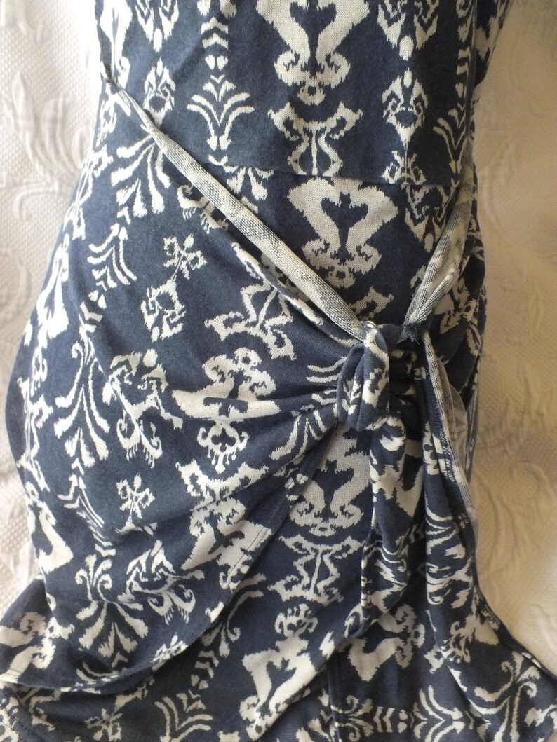 May include: A navy blue wrap dress with a white floral pattern. The dress is tied at the waist with a matching fabric belt. The fabric is soft and flowing, perfect for a summer day.