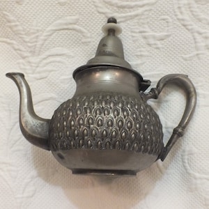 May include: A silver teapot with a textured, patterned body and a lid with a small knob on top. The teapot has a spout and a handle.