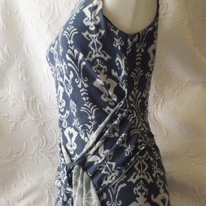May include: A sleeveless, navy blue dress with a white, ornate pattern. The dress features a knot detail at the waist, creating a draped effect. The fabric appears soft and flowing, suitable for warm weather.