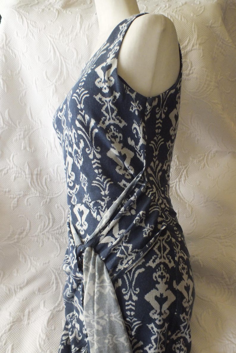 May include: A sleeveless, navy blue dress with a white, ornate pattern. The dress features a knot detail at the waist, creating a draped effect. The fabric appears soft and flowing, suitable for warm weather.