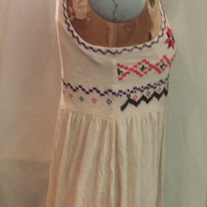 May include: A white sleeveless top with a geometric pattern embroidered in purple, red, and black thread.