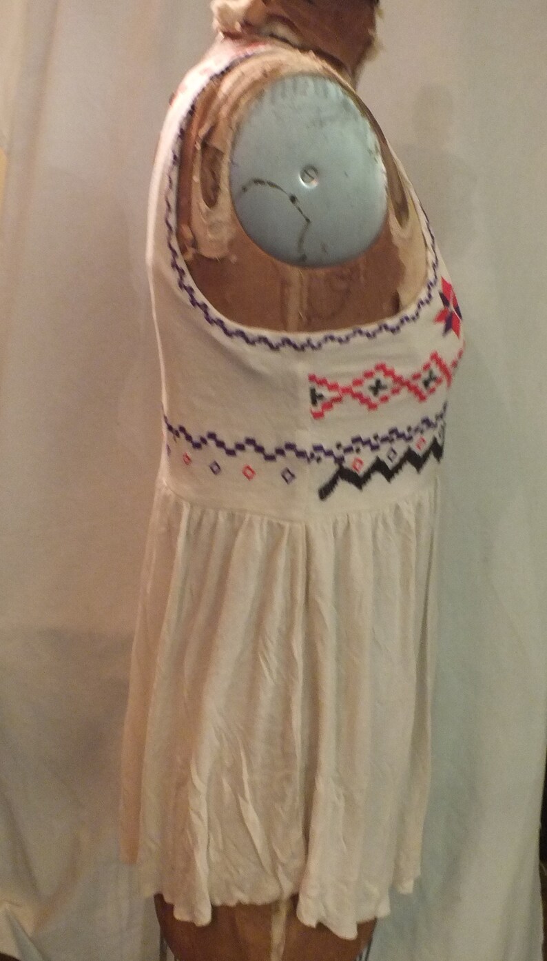 May include: A white sleeveless top with a geometric pattern embroidered in purple, red, and black thread.