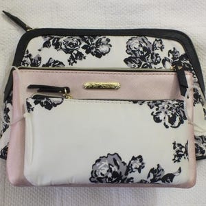 May include: A white and black floral print makeup bag with a pink zippered pouch and a smaller white and black floral print pouch inside. The bag has a black zipper and a gold zipper pull.