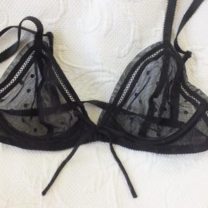 May include: Black lace lingerie bra with polka dots. The bra has adjustable straps and a tie closure in the front.