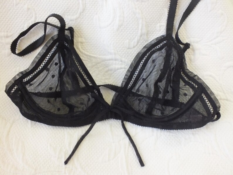 May include: Black lace lingerie bra with polka dots. The bra has adjustable straps and a tie closure in the front.