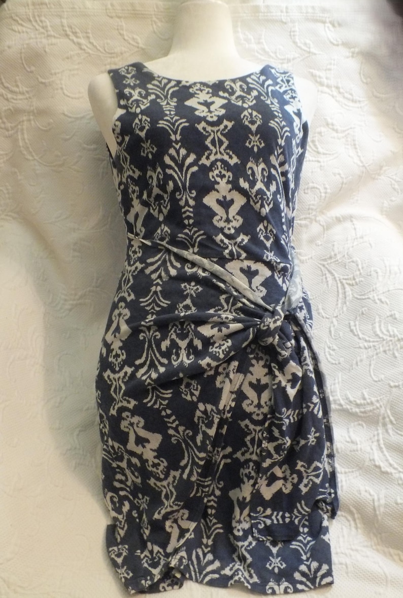 May include: Sleeveless navy blue dress with a white damask pattern. The dress features a knotted detail at the waist. The dress is displayed on a mannequin.
