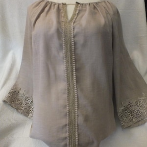 Puede incluir: Una blusa beige con cuello en V y ribete de encaje en las mangas y en la parte delantera.