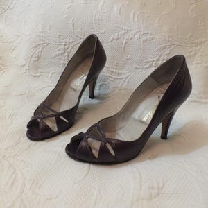 May include: A pair of purple peep-toe heels with a cut-out design. The heels are made of leather and have a stiletto heel.