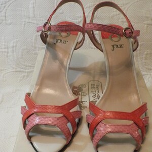 May include: Pair of Jour brand open-toe high-heeled sandals. The sandals feature a strappy design with a mix of pink and coral-colored faux snakeskin material. The heels are approximately 3 inches high. The word "jour" is printed on the insole.