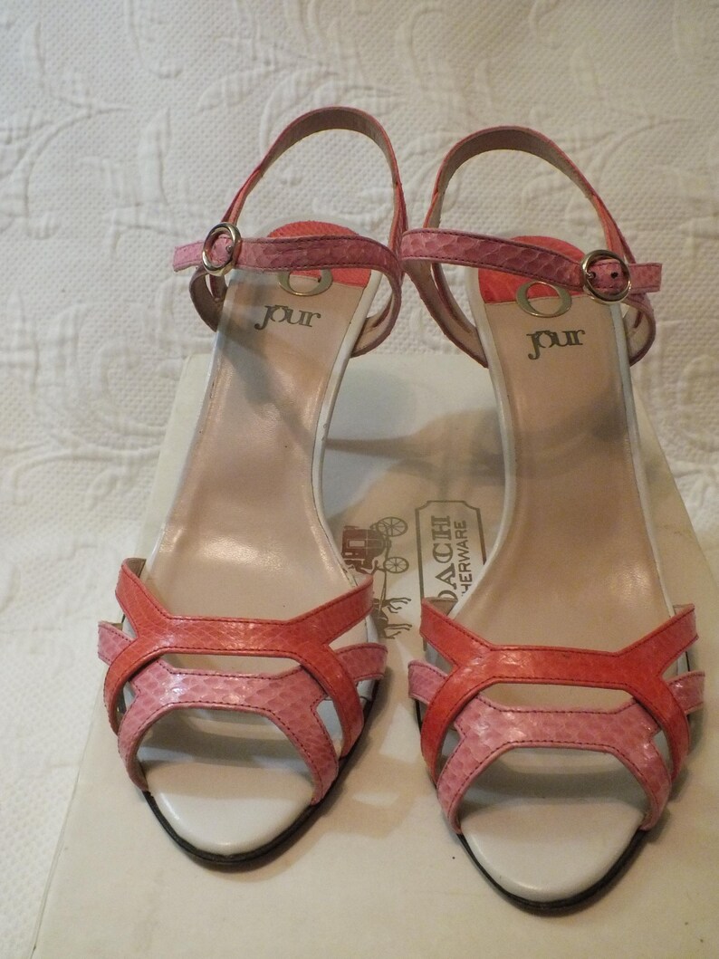 May include: Pair of Jour brand open-toe high-heeled sandals. The sandals feature a strappy design with a mix of pink and coral-colored faux snakeskin material. The heels are approximately 3 inches high. The word "jour" is printed on the insole.