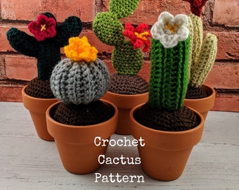 May include: Five crocheted cactus plants in terracotta pots. The cacti are different colors and shapes, including a green prickly pear cactus, a gray barrel cactus, a green columnar cactus, and two green cacti with red flowers. The cacti are arranged on a white wooden surface. Crochet Cactus Pattern.