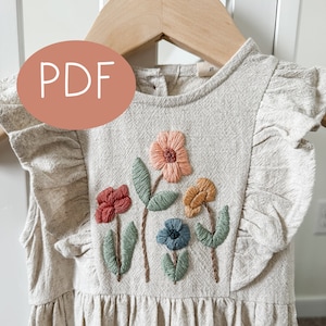May include: A beige linen dress with embroidered flowers in shades of orange, red, blue, and green. The dress has a ruffled neckline and sleeves.